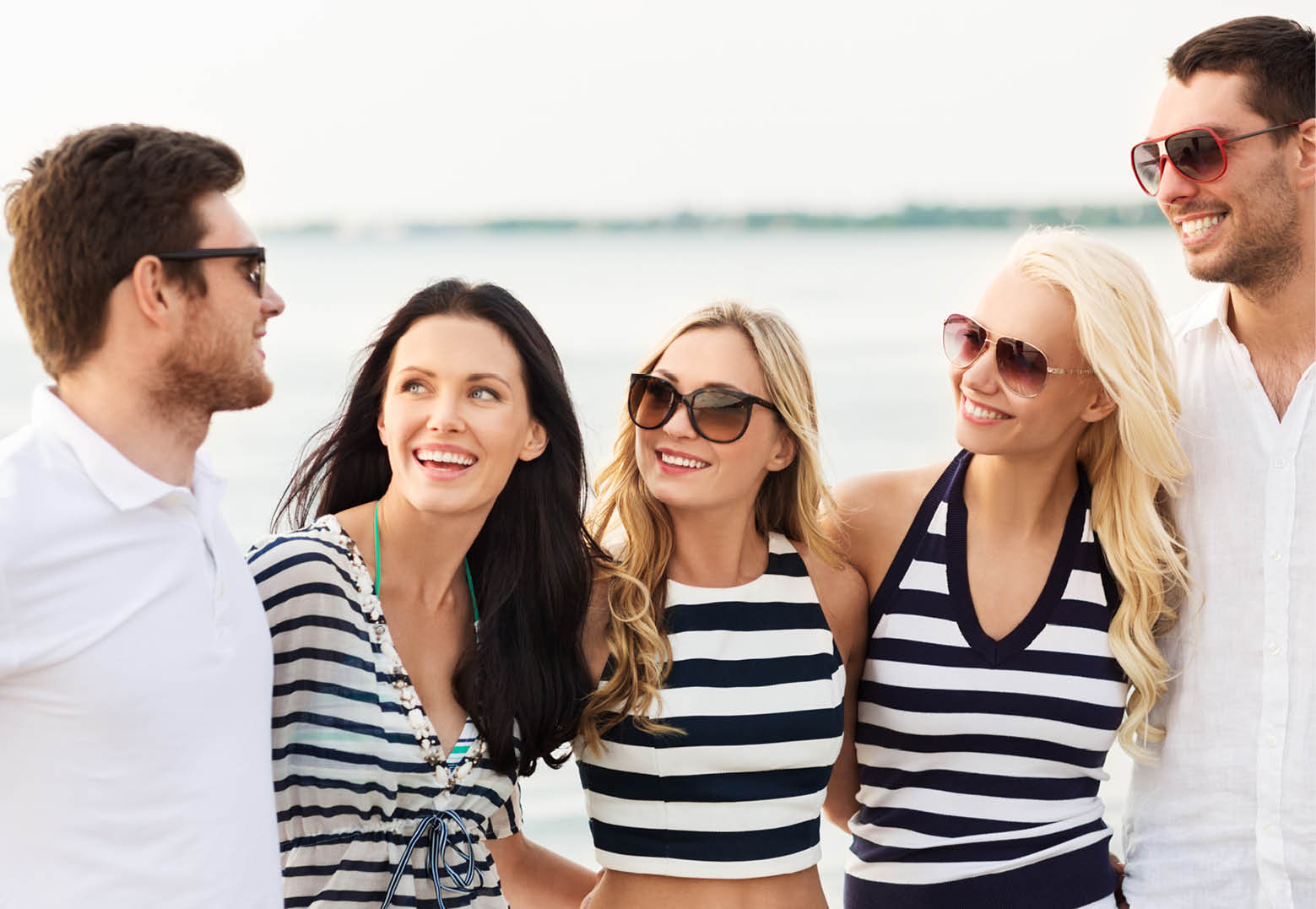 friendship, summer holidays and people concept - group of happy friends in striped clothes on beach